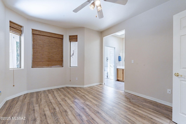 spare room featuring light wood-type flooring, a ceiling fan, and baseboards