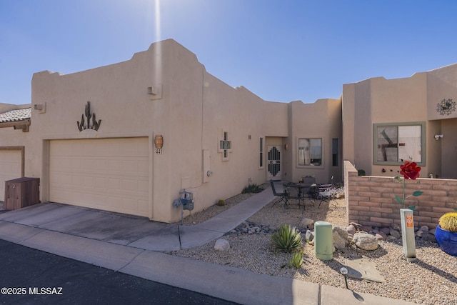 pueblo-style home featuring an attached garage, concrete driveway, and stucco siding