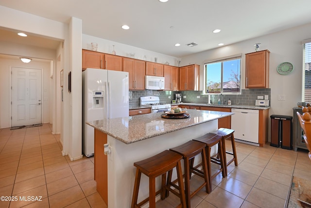 kitchen with sink, backsplash, a kitchen bar, a center island, and white appliances