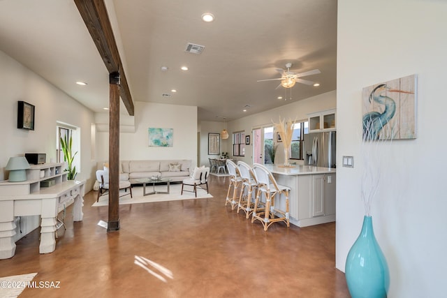 interior space with concrete flooring, a breakfast bar area, ceiling fan, and stainless steel fridge with ice dispenser