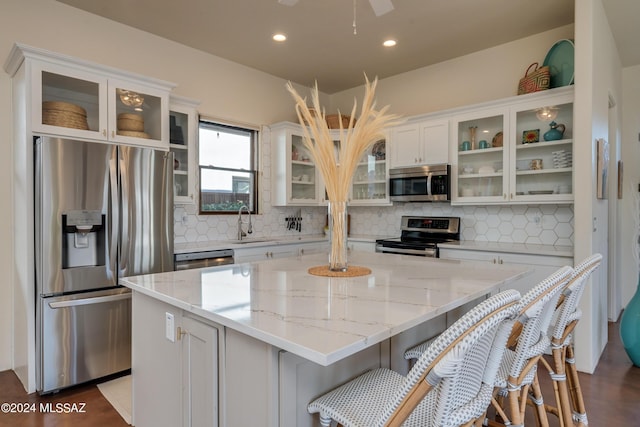 kitchen featuring backsplash, stainless steel appliances, light stone counters, white cabinets, and a kitchen island