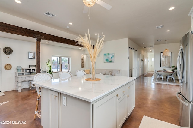 kitchen featuring a breakfast bar area, stainless steel fridge, white cabinets, a barn door, and light stone countertops