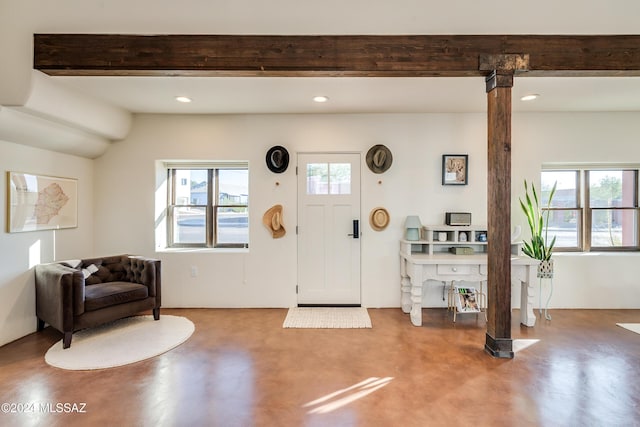 foyer featuring beamed ceiling, concrete flooring, and a wealth of natural light