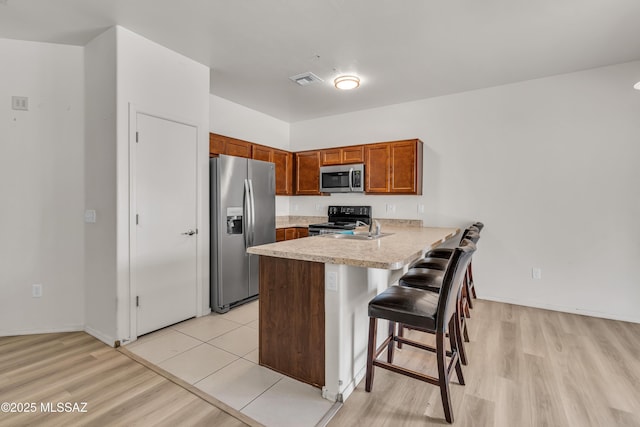 kitchen featuring a kitchen bar, light wood-type flooring, kitchen peninsula, and appliances with stainless steel finishes