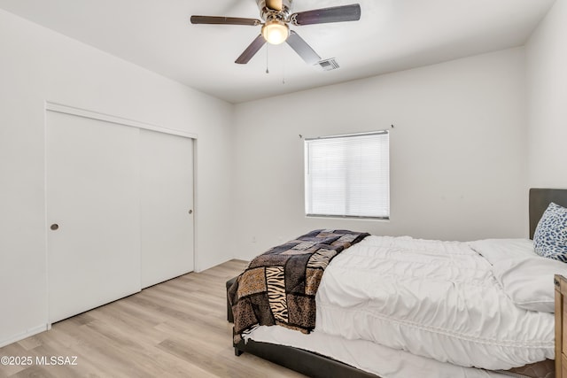 bedroom with light wood-type flooring, ceiling fan, and a closet