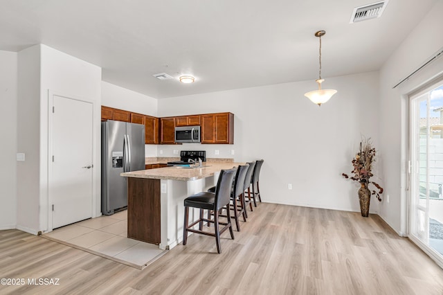 kitchen with light stone counters, decorative light fixtures, appliances with stainless steel finishes, a kitchen breakfast bar, and light hardwood / wood-style floors