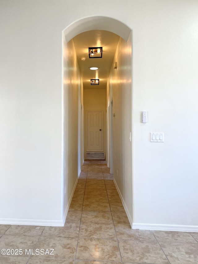 hall with arched walkways, light tile patterned floors, and baseboards