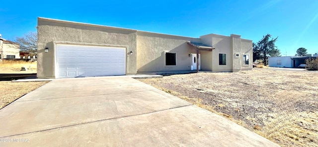 pueblo-style house with driveway, an attached garage, and stucco siding