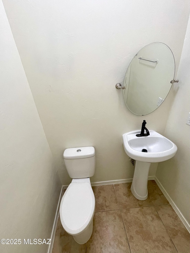 half bath with toilet, baseboards, and tile patterned floors