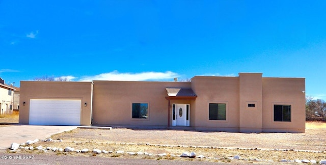 pueblo-style home with a garage, concrete driveway, and stucco siding