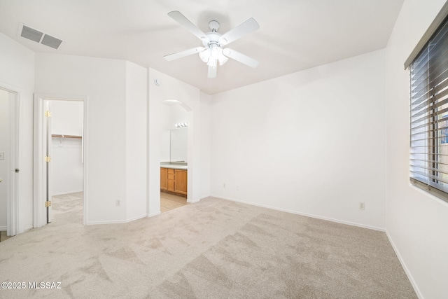 unfurnished bedroom featuring ensuite bathroom, a spacious closet, light colored carpet, ceiling fan, and a closet