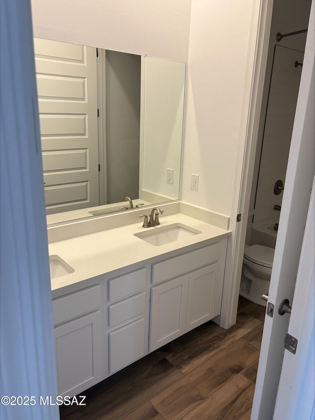 full bathroom featuring wood finished floors, toilet, double vanity, and a sink