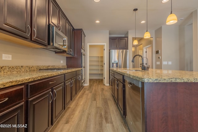 kitchen featuring hanging light fixtures, stainless steel appliances, dark brown cabinetry, light hardwood / wood-style floors, and a center island with sink