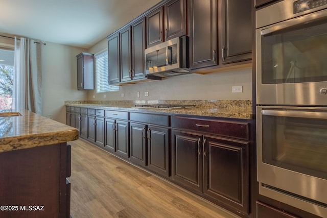 kitchen with light stone counters, dark brown cabinetry, appliances with stainless steel finishes, and light hardwood / wood-style floors