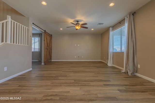 spare room featuring wood-type flooring, a barn door, and ceiling fan