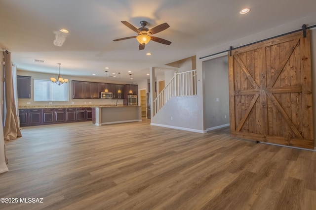 unfurnished living room featuring ceiling fan with notable chandelier, a barn door, and hardwood / wood-style floors