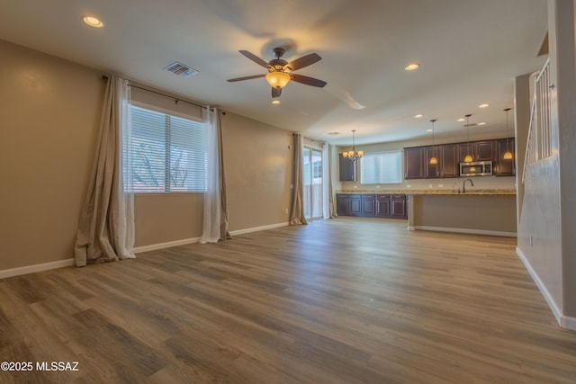 unfurnished living room featuring wood-type flooring, sink, and ceiling fan with notable chandelier