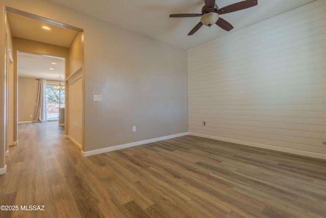 unfurnished room with ceiling fan with notable chandelier, hardwood / wood-style floors, and wooden walls