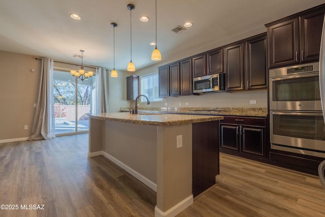 kitchen with sink, light stone counters, dark brown cabinets, appliances with stainless steel finishes, and pendant lighting