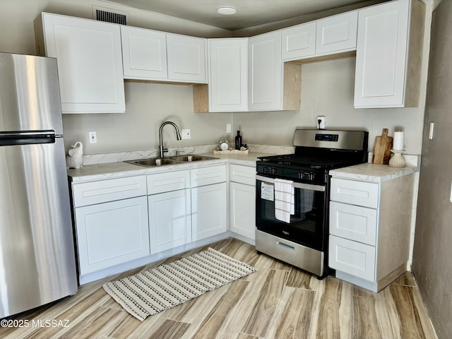 kitchen with white cabinetry, stainless steel appliances, sink, and light wood-type flooring