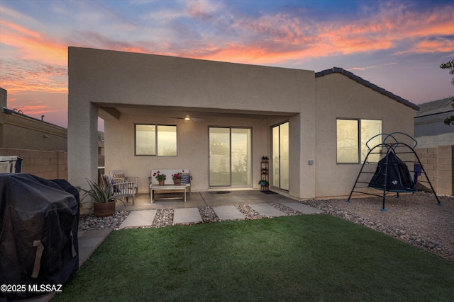 back house at dusk featuring a patio and a lawn