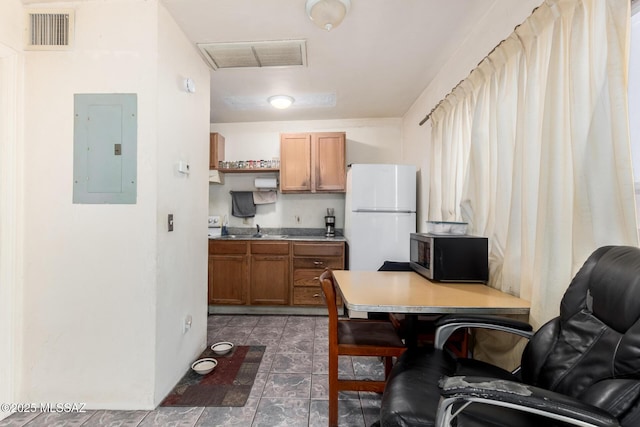 kitchen with visible vents, brown cabinets, electric panel, stainless steel microwave, and freestanding refrigerator