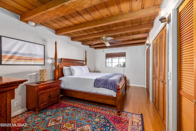 bedroom with beam ceiling, two closets, light wood finished floors, baseboards, and wood ceiling