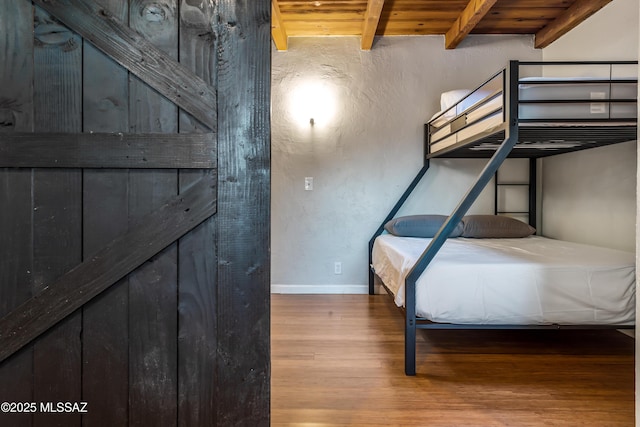 unfurnished bedroom with baseboards, wood finished floors, beam ceiling, wooden ceiling, and a textured wall