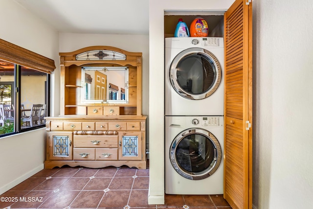 clothes washing area featuring laundry area, stacked washer and clothes dryer, baseboards, and dark tile patterned flooring