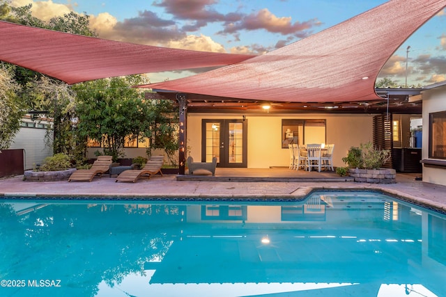 pool at dusk featuring an outdoor pool, french doors, and a patio