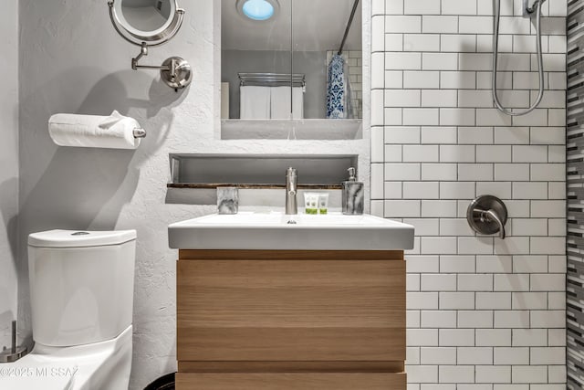 full bathroom with vanity, toilet, a textured wall, and a tile shower