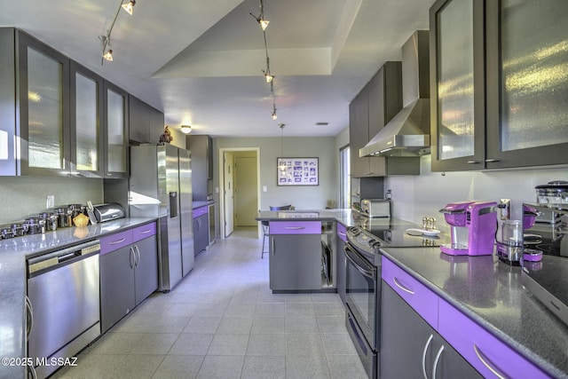 kitchen with rail lighting, hanging light fixtures, stainless steel appliances, dark stone counters, and wall chimney exhaust hood