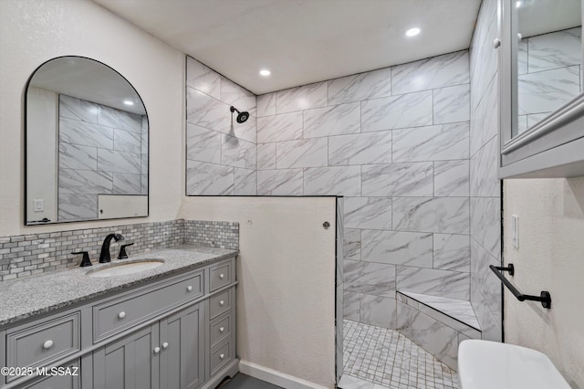 bathroom featuring vanity, tiled shower, and backsplash