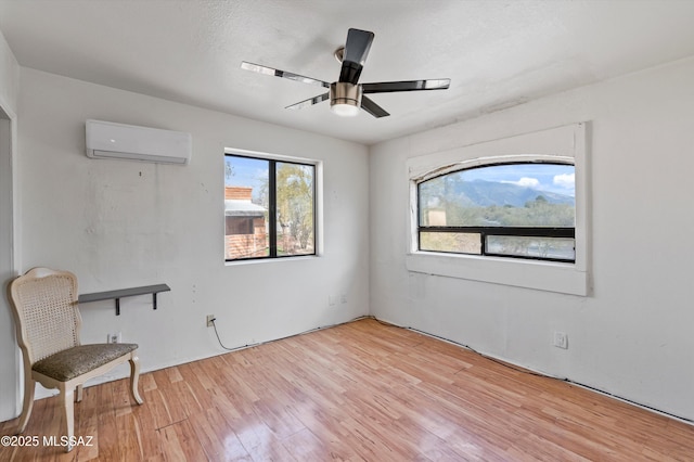 spare room featuring ceiling fan, a wall mounted AC, and light wood-type flooring