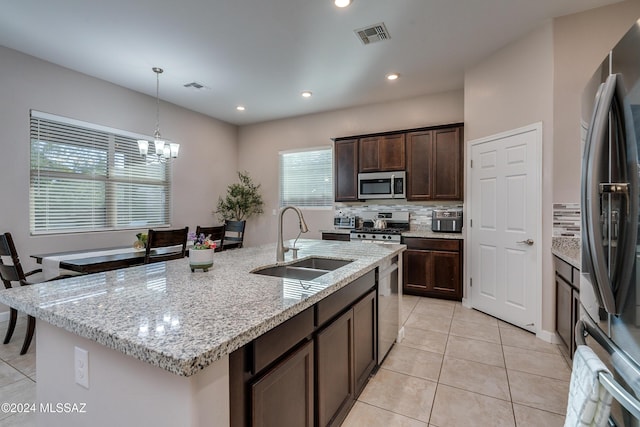 kitchen featuring sink, a chandelier, stainless steel appliances, light stone countertops, and a center island with sink