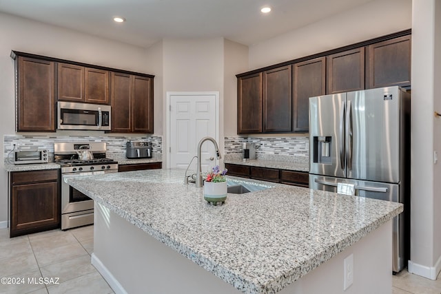 kitchen featuring light tile patterned flooring, an island with sink, sink, stainless steel appliances, and light stone countertops