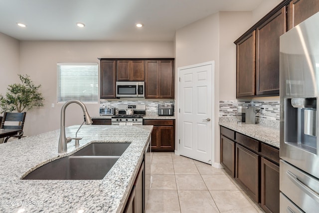 kitchen featuring dark brown cabinetry, sink, light stone counters, light tile patterned floors, and appliances with stainless steel finishes