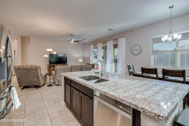 kitchen with sink, light stone counters, light tile patterned floors, appliances with stainless steel finishes, and an island with sink