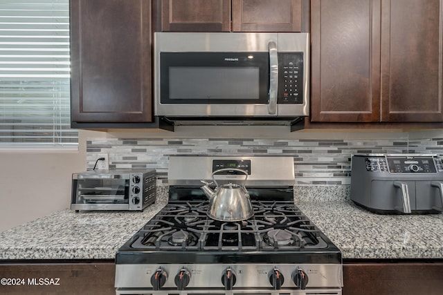 kitchen featuring appliances with stainless steel finishes, light stone counters, backsplash, and dark brown cabinetry