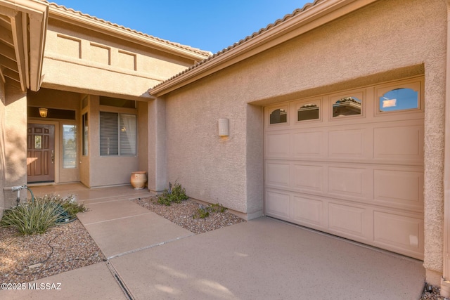 view of exterior entry featuring a garage, a tiled roof, and stucco siding