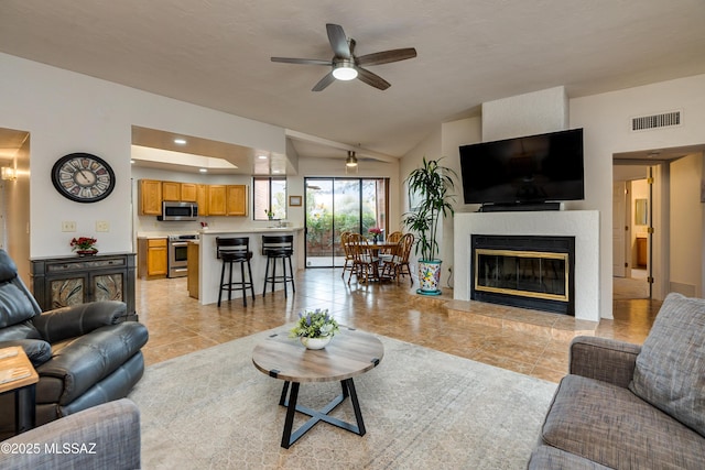 tiled living room featuring a tiled fireplace, vaulted ceiling, and ceiling fan