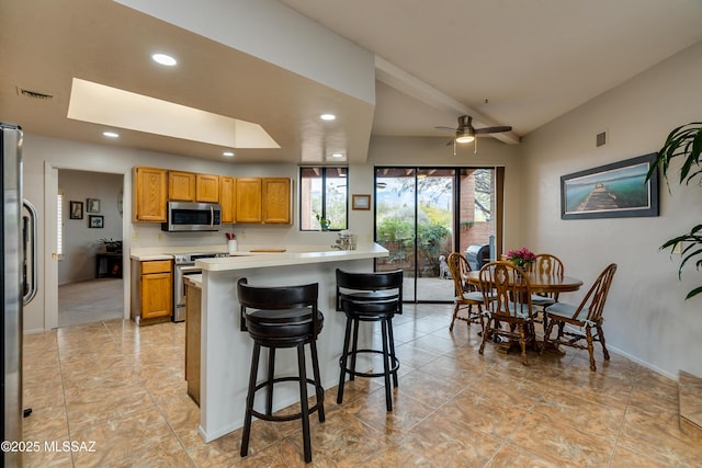 kitchen with ceiling fan, stainless steel appliances, a kitchen breakfast bar, and lofted ceiling with skylight