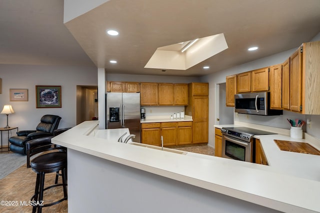 kitchen with a skylight, sink, a breakfast bar area, kitchen peninsula, and stainless steel appliances