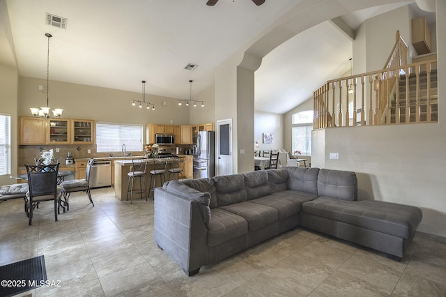 living room with sink, ceiling fan with notable chandelier, high vaulted ceiling, and a healthy amount of sunlight