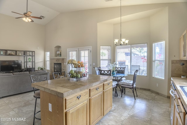 kitchen with ceiling fan with notable chandelier, a breakfast bar, a kitchen island, decorative light fixtures, and light tile patterned flooring