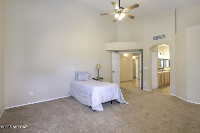 carpeted bedroom with connected bathroom, ceiling fan, and a high ceiling