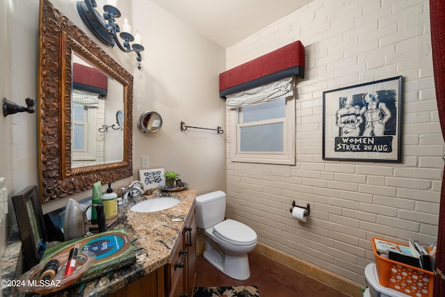 bathroom with vanity, toilet, and brick wall