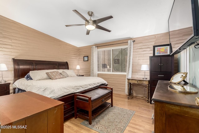 bedroom with ceiling fan, vaulted ceiling, brick wall, and light wood-type flooring