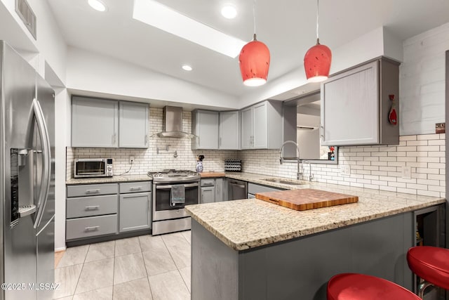 kitchen with sink, decorative light fixtures, kitchen peninsula, stainless steel appliances, and wall chimney range hood