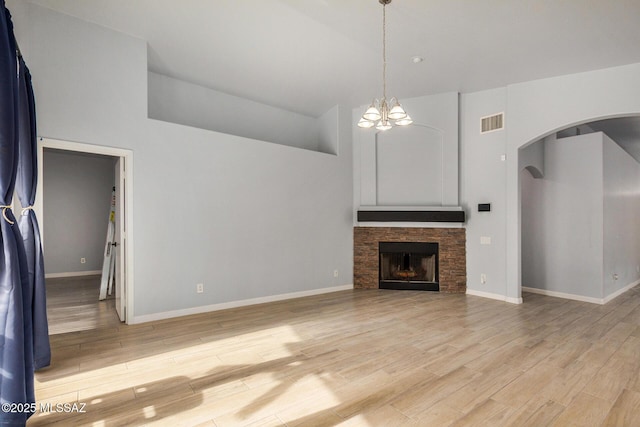 unfurnished living room with a notable chandelier, a stone fireplace, light hardwood / wood-style floors, and high vaulted ceiling